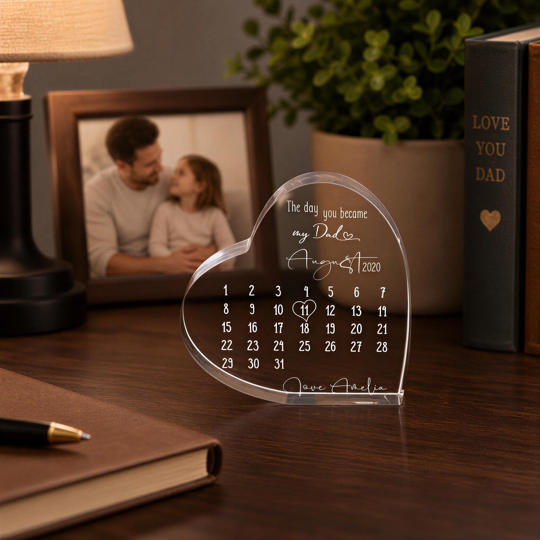 a heart-shaped photo frame with a calendar inside, placed on a wooden desk. The frame has a photo of a man and a girl inside, and the calendar displays the day "August 8, 2020".