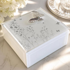 A white box with a floral design and a silver butterfly decoration on top, placed on a marble surface.