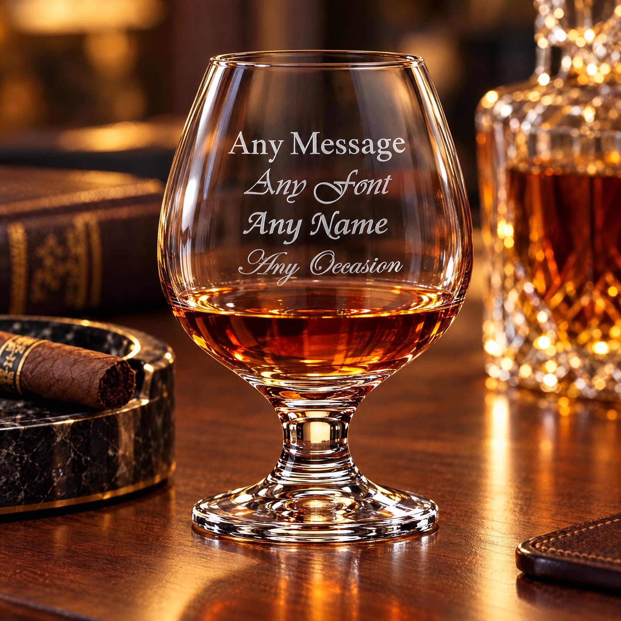 A personalized glass of whiskey with the inscription "Any Message Any Font Any Name Any Occasion" engraved on it, placed on a wooden surface with a cigar and a bottle of whiskey in the background.