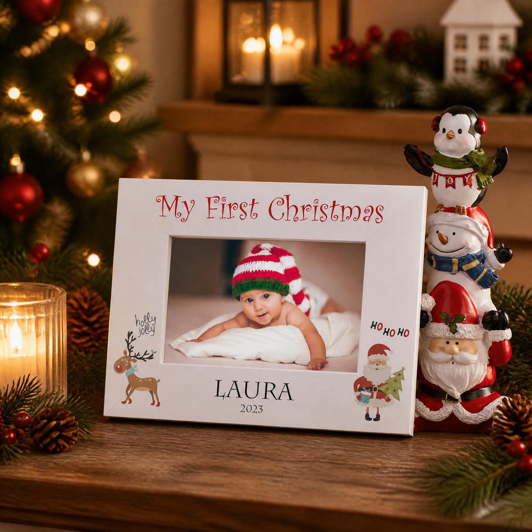 A white picture frame with a photo of a baby and the text "My First Christmas" is displayed on a wooden surface, surrounded by Christmas decorations and a small figurine of Santa Claus.