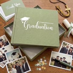a graduation celebration, with a graduation cap and tassel, a graduation gown, and a graduation book with a graduation cap and tassel. There are also graduation photos and a pen on a wooden surface.