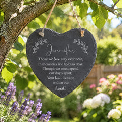 A heart-shaped slate hanging from a tree branch with a personal message engraved on it.