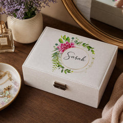 A white jewelry box with a floral design and the name "Sarah" printed on it, placed on a wooden surface next to a mirror and some decorative items.