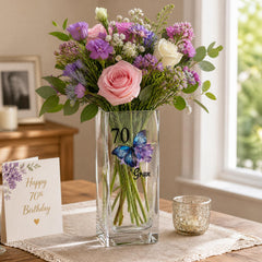 A bouquet of colorful flowers in a clear glass vase, placed on a table next to a card with a message and a small candle.