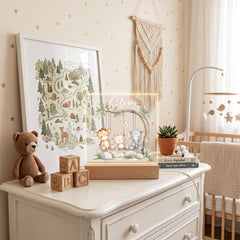 A nursery room with a white dresser, a wooden block display with alphabet blocks, a framed picture of animals, a hanging wall decoration, a baby crib, and a potted plant.