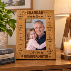 A wooden picture frame with a photo of a man and a young girl, surrounded by various books and a candle on a wooden surface.