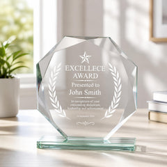 A clear glass award trophy with a star and laurel wreath design, placed on a glass stand. The trophy is presented to John Smith for an Excellence Award.