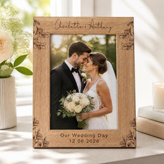 A wooden picture frame with a bride and groom in the center, holding a bouquet of flowers, and the text "Our Wedding Day 12.06.2026" engraved on it.