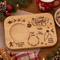 A wooden tray with a carved design and text, surrounded by Christmas decorations and a mug of milk.