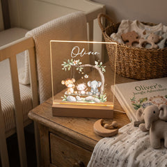 A wooden nightstand with a lighted picture frame containing a picture of a baby elephant, a baby giraffe, and a baby monkey, along with a wooden rocking horse and a wooden toy elephant. The nightstand is situated next to a basket filled with baby toys.