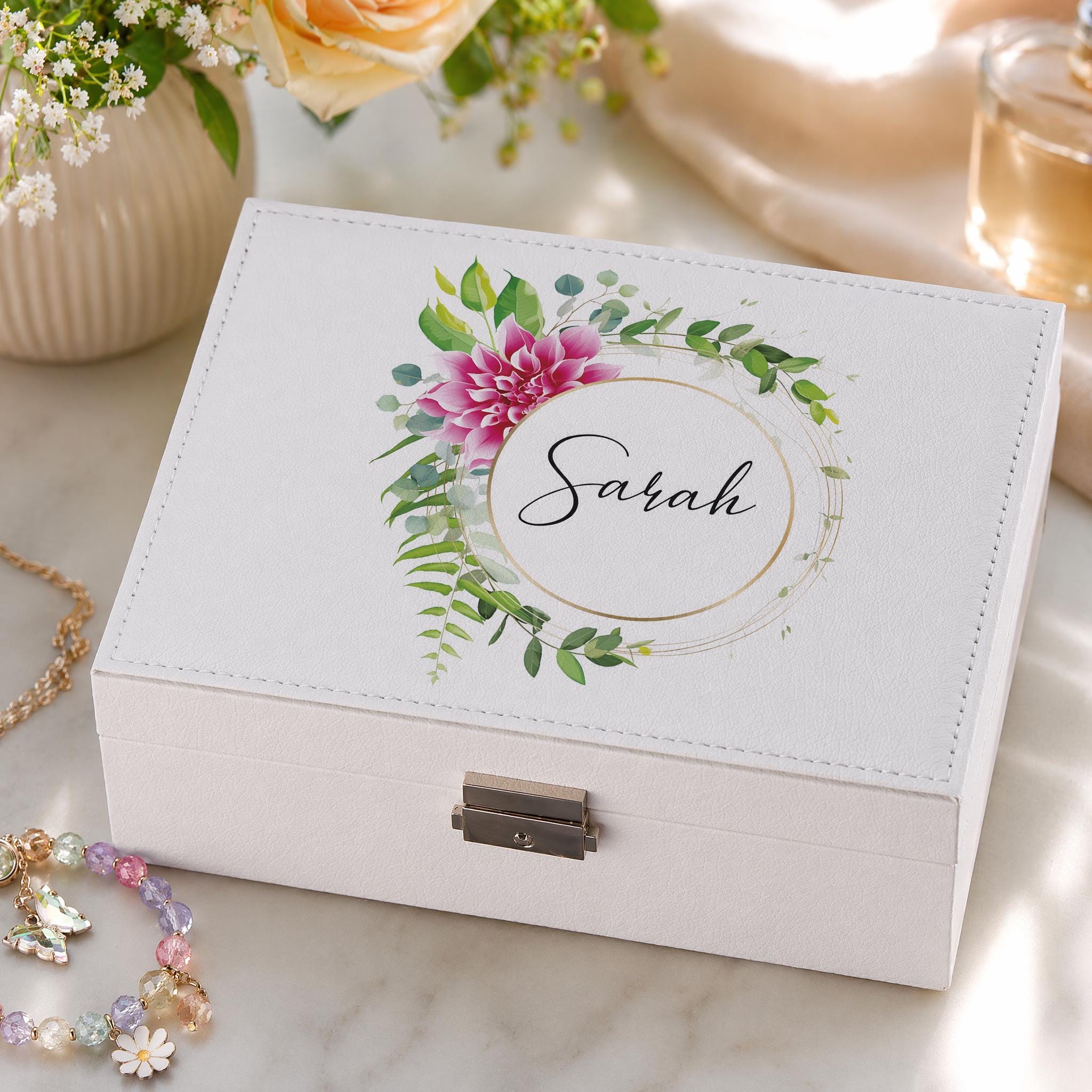 A white jewelry box with a floral design and the name "Sarah" printed on it, placed on a marble surface.