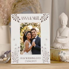 A white wedding picture frame with a couple in a romantic pose, surrounded by decorative elements such as a Buddha statue, a vase, and a candle.