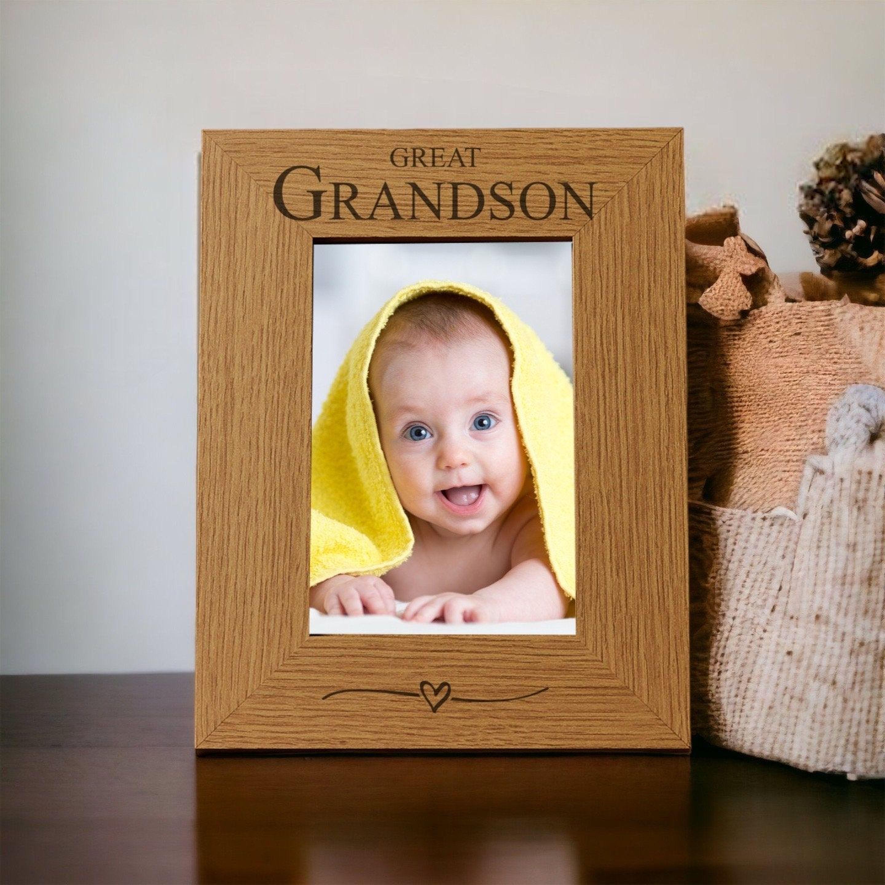 A wooden picture frame with a photo of a smiling baby wrapped in a yellow towel inside it, placed on a wooden surface next to a beige blanket.