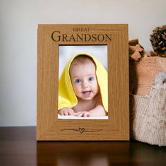 A wooden picture frame with a photo of a smiling baby wrapped in a yellow towel inside it, placed on a wooden surface next to a beige blanket.