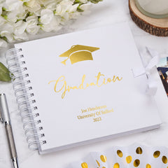 a graduation cap and a graduation cap-themed notebook with the word "Graduation" written on it, placed on a marble surface.