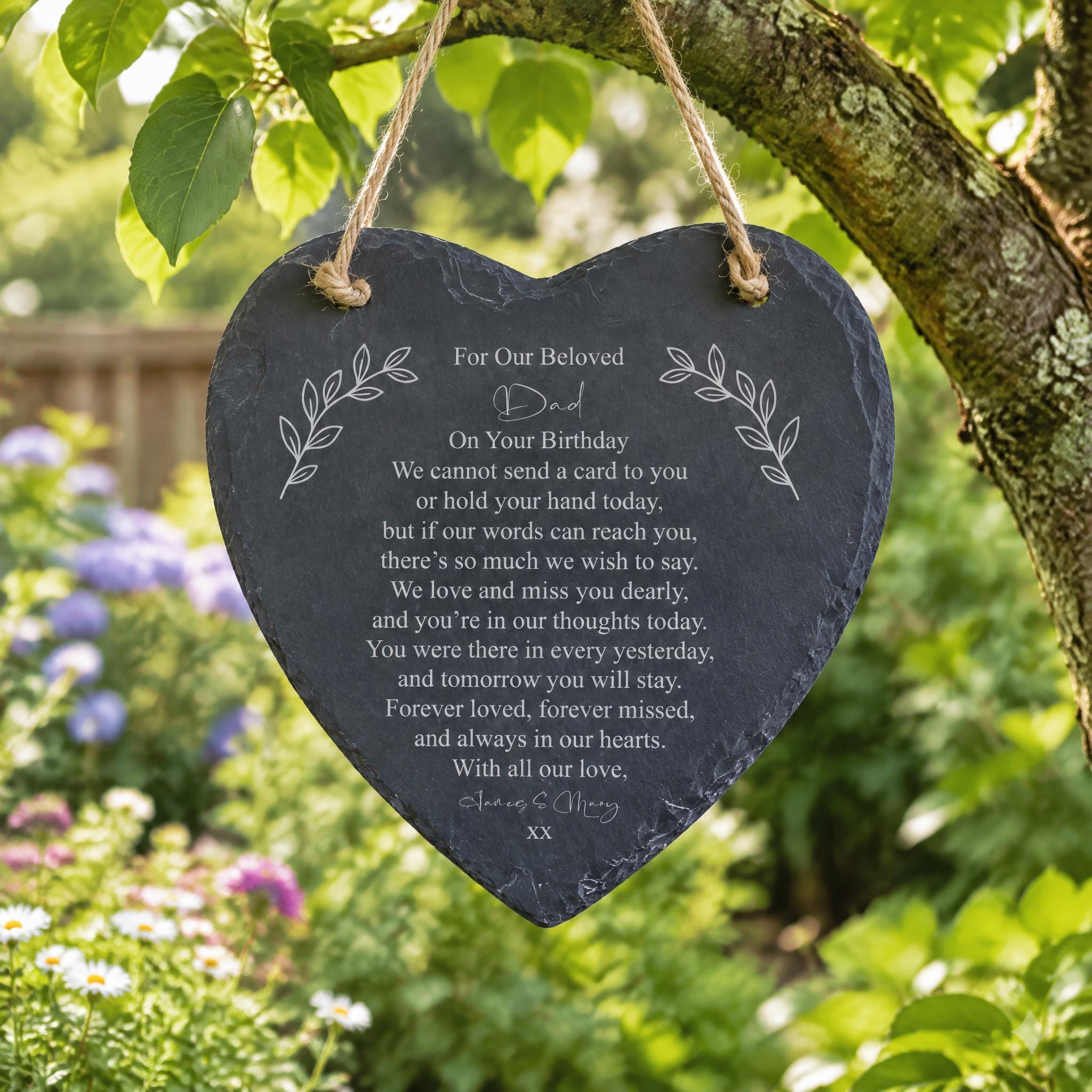 A heart-shaped slate hanging from a tree branch with a heartfelt message written on it.