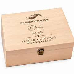 A wooden box with a lid, engraved with the text "CHERISHED MEMORIES OF Dad 1945-2026 A LITTLE BOX OF MEMORIES, A LIFETIME OF LOVE" and a feather design.