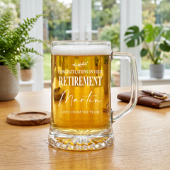 A glass mug filled with beer, placed on a wooden table, with a personalized message that congratulates someone on their retirement.