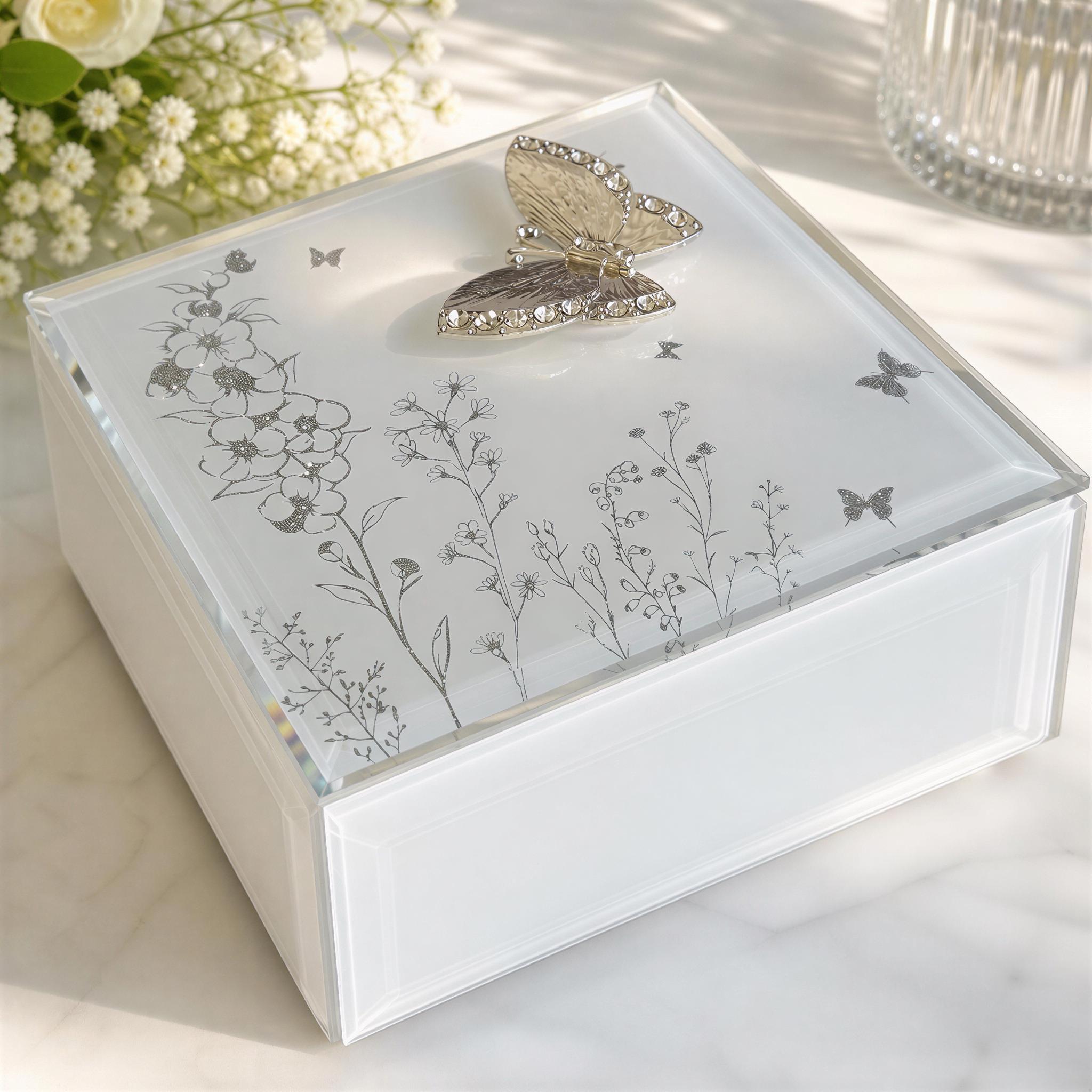 A decorative glass box with a butterfly motif, featuring a floral and plant design, sits on a marble surface.
