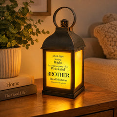 A black lantern with a yellow light on it sits on a wooden table, accompanied by a stack of books and a potted plant.