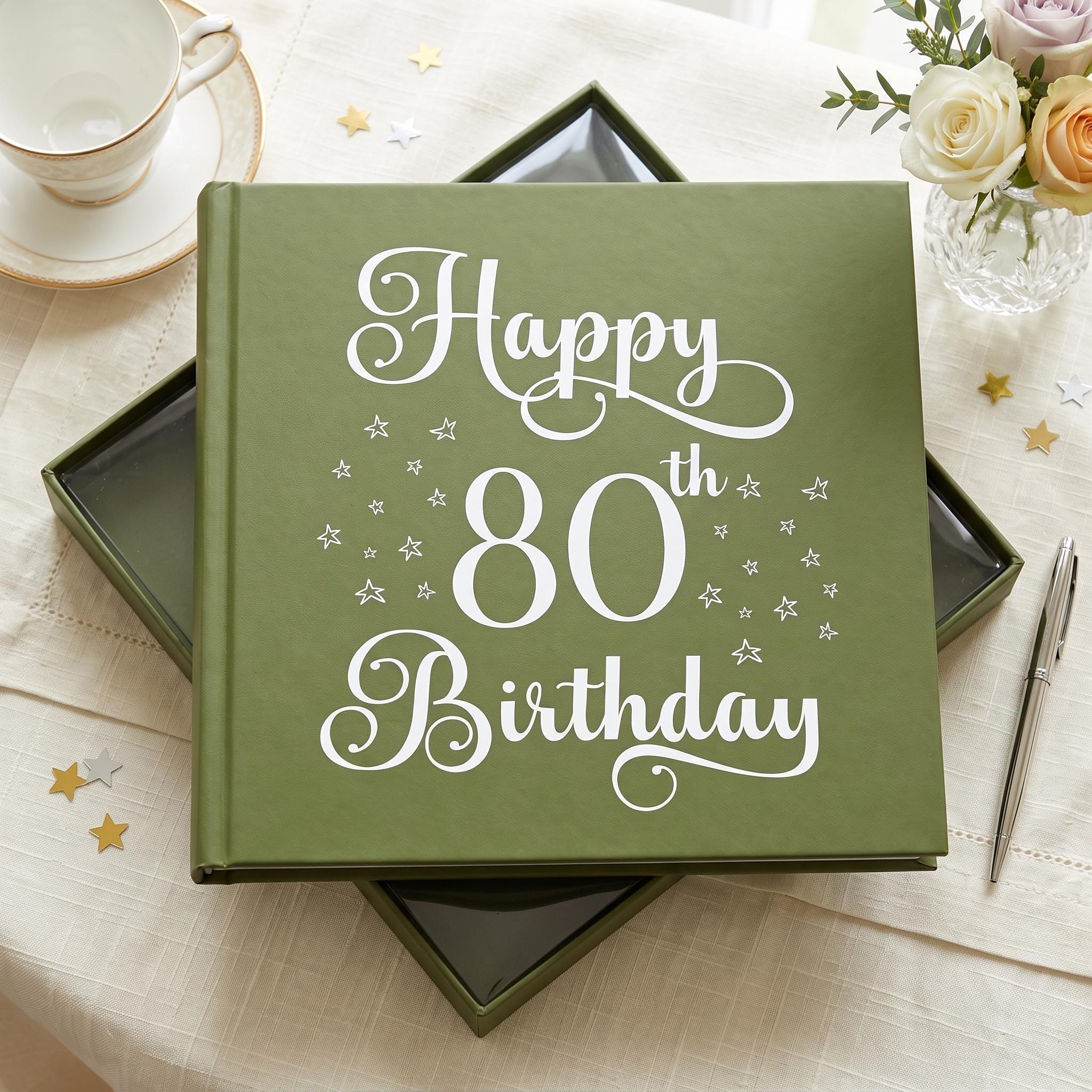 A green book titled "Happy 80th Birthday" sits on a table, surrounded by a teacup, a vase of flowers, and scattered gold stars.