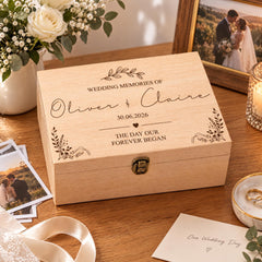 A wooden box with a personalized inscription, surrounded by wedding-related items such as photographs, a ribbon, and a candle.