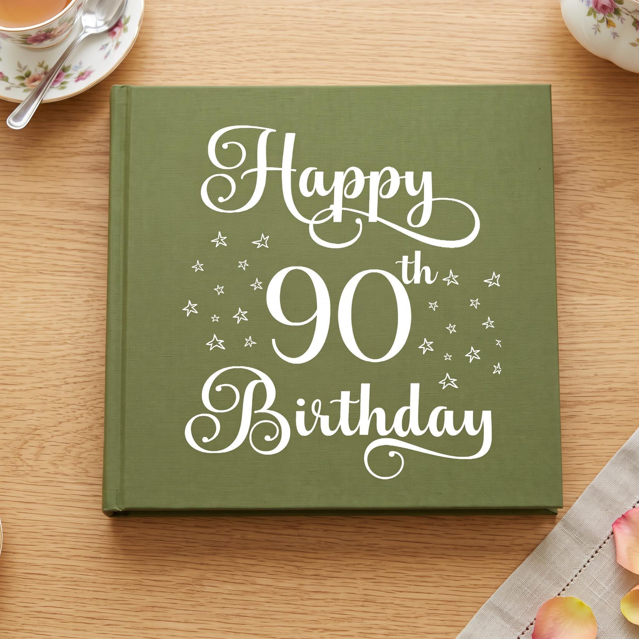 A green book titled "Happy 90th Birthday" with white text and star decorations on a wooden surface.
