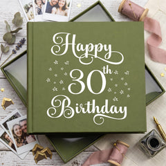 a green book with the text "Happy 30th Birthday" on it, surrounded by various items such as photographs, ribbons, and stationery.