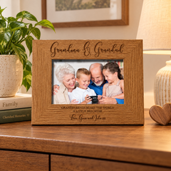 A wooden picture frame containing a family photo of a man, woman, and two children, with the text "Grandma & Grandpa" and "Grandparents make the world a little brighter" engraved on the frame.