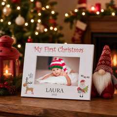 A white picture frame with a photo of a baby and holiday decorations, including a gnome figurine, a Christmas tree, and a red lantern, all set against a background of twinkling lights.