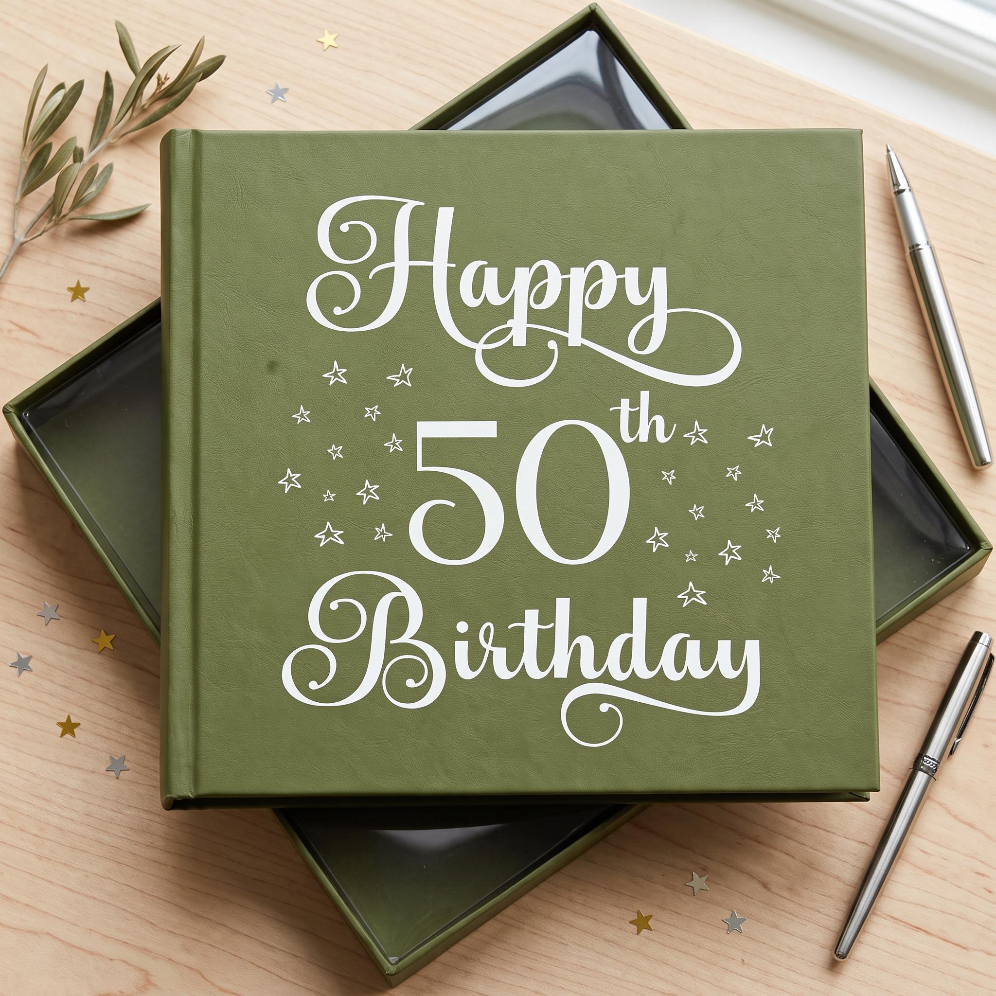 A green book titled "Happy 50th Birthday" with white text and stars on the cover, placed on a wooden surface with a pen and some gold stars.