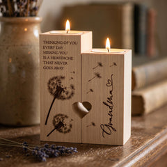 A wooden candle holder with a dandelion design and the text "Thinking of you every day. Missing you is a heartache that never goes away" on it, placed on a wooden surface.