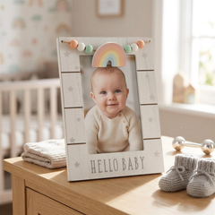 A wooden picture frame with a baby's photo inside, placed on a wooden dresser next to baby booties and a stuffed animal.