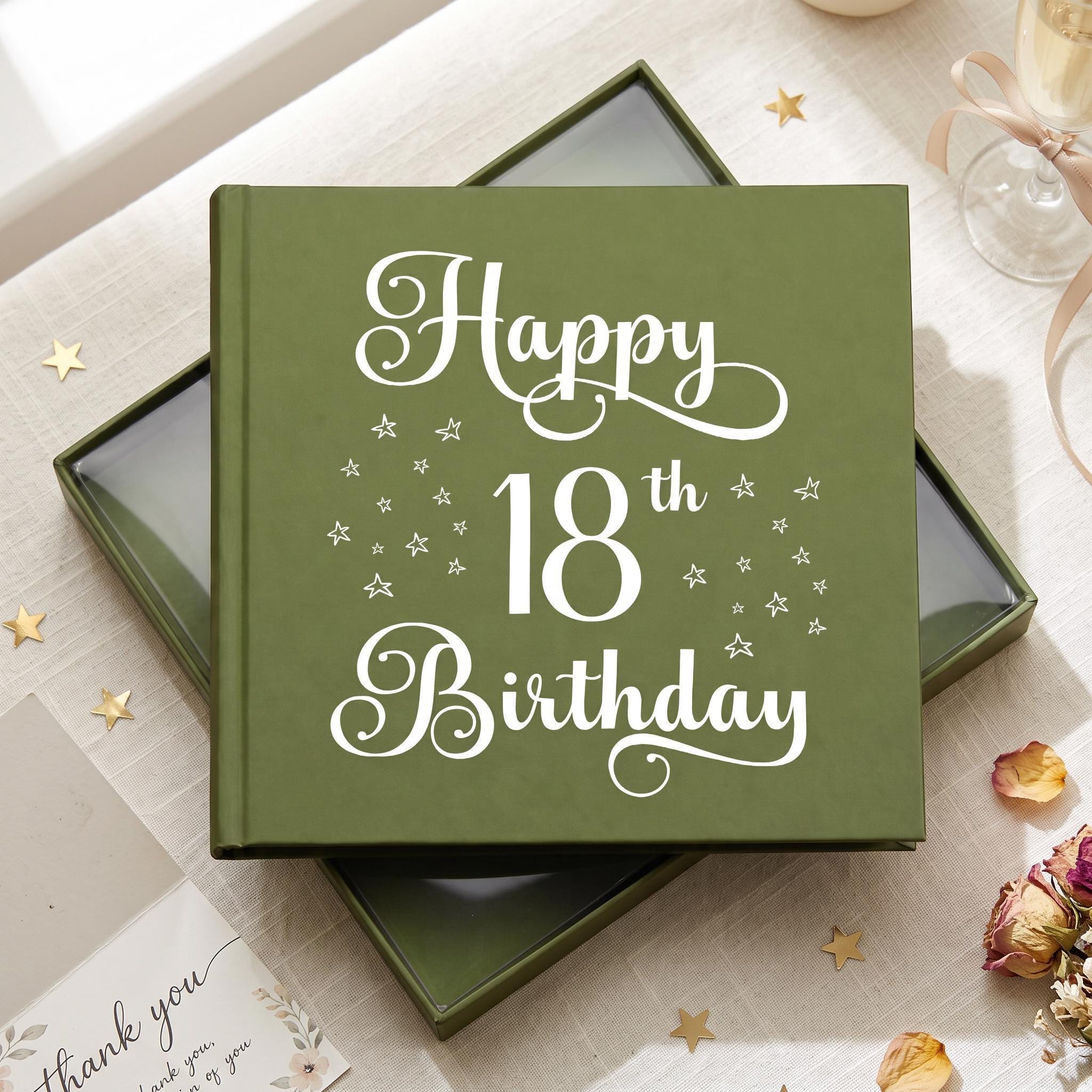 A green box with a white inscription that reads "Happy 18th Birthday" is placed on a table with a glass of wine and some flowers.
