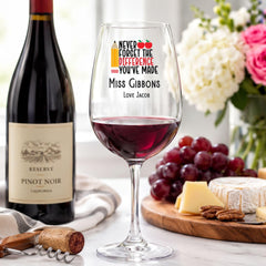 a wine glass with a personalized message, a bottle of wine, and a cheese platter with grapes and cheese.