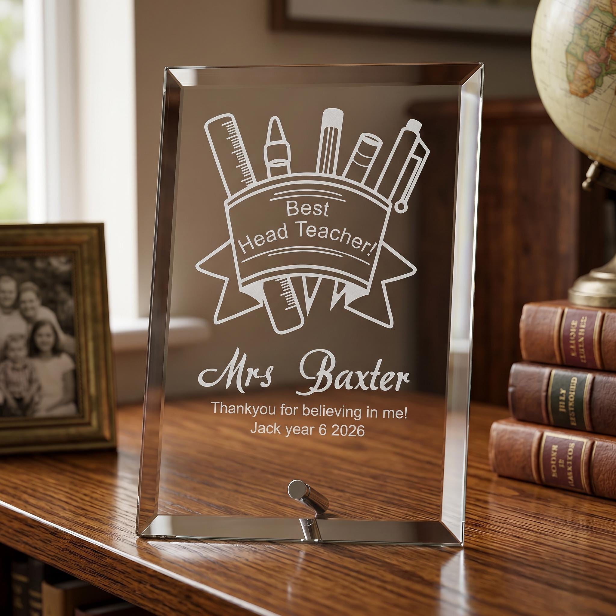 A glass picture frame with a personalized message engraved on it, placed on a wooden surface.