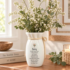 A white vase with a floral arrangement sits on a wooden surface, accompanied by a book titled "The Kinfolk Home" and a candle holder.