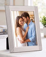 A couple embracing each other in a white picture frame on a table.