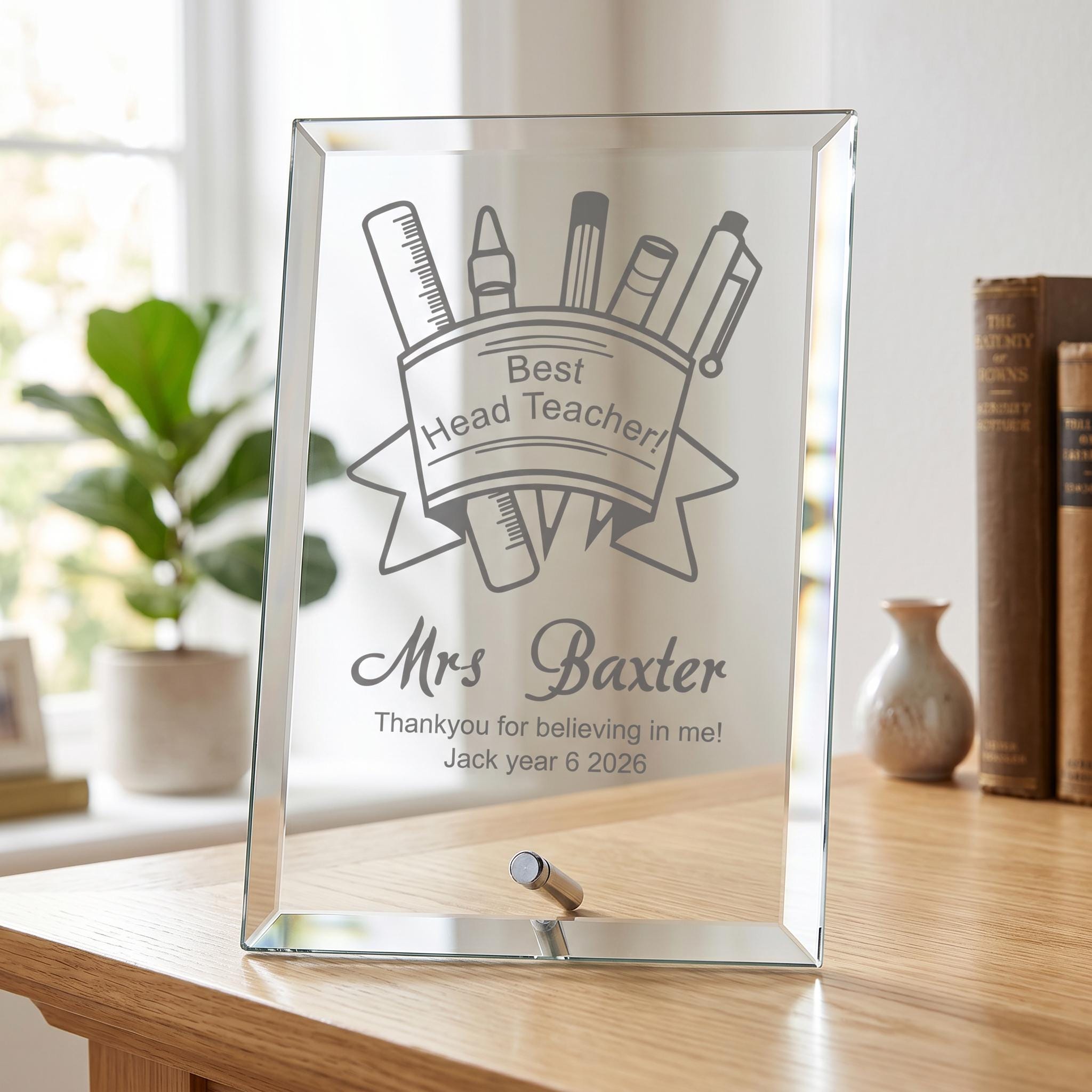 A glass frame with a personalized message engraved on it, placed on a wooden desk.