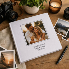 a white photo album with a couple embracing, surrounded by various photography equipment and a candle on a wooden surface.