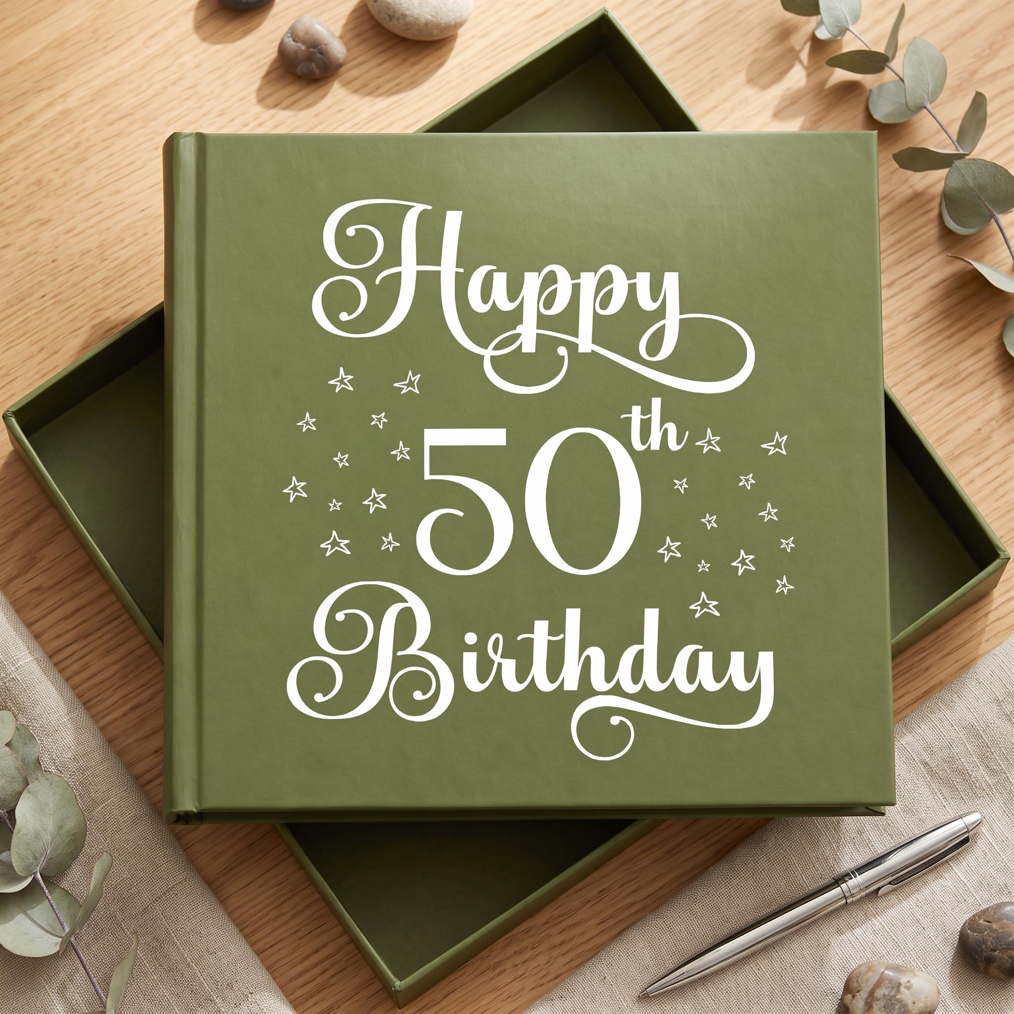 A green book titled "Happy 50th Birthday" with white text and stars on the cover, placed on a wooden surface with some rocks and greenery in the background.