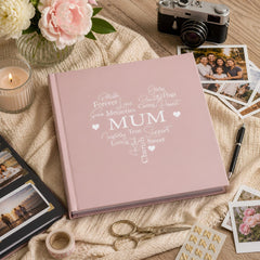 A pink photo album with the word "MUM" printed on it, surrounded by various items such as a camera, photographs, and a candle.
