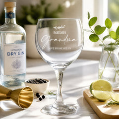 a clear wine glass with a personalized message, a bottle of London Dry Gin, and some fresh lime slices on a table.