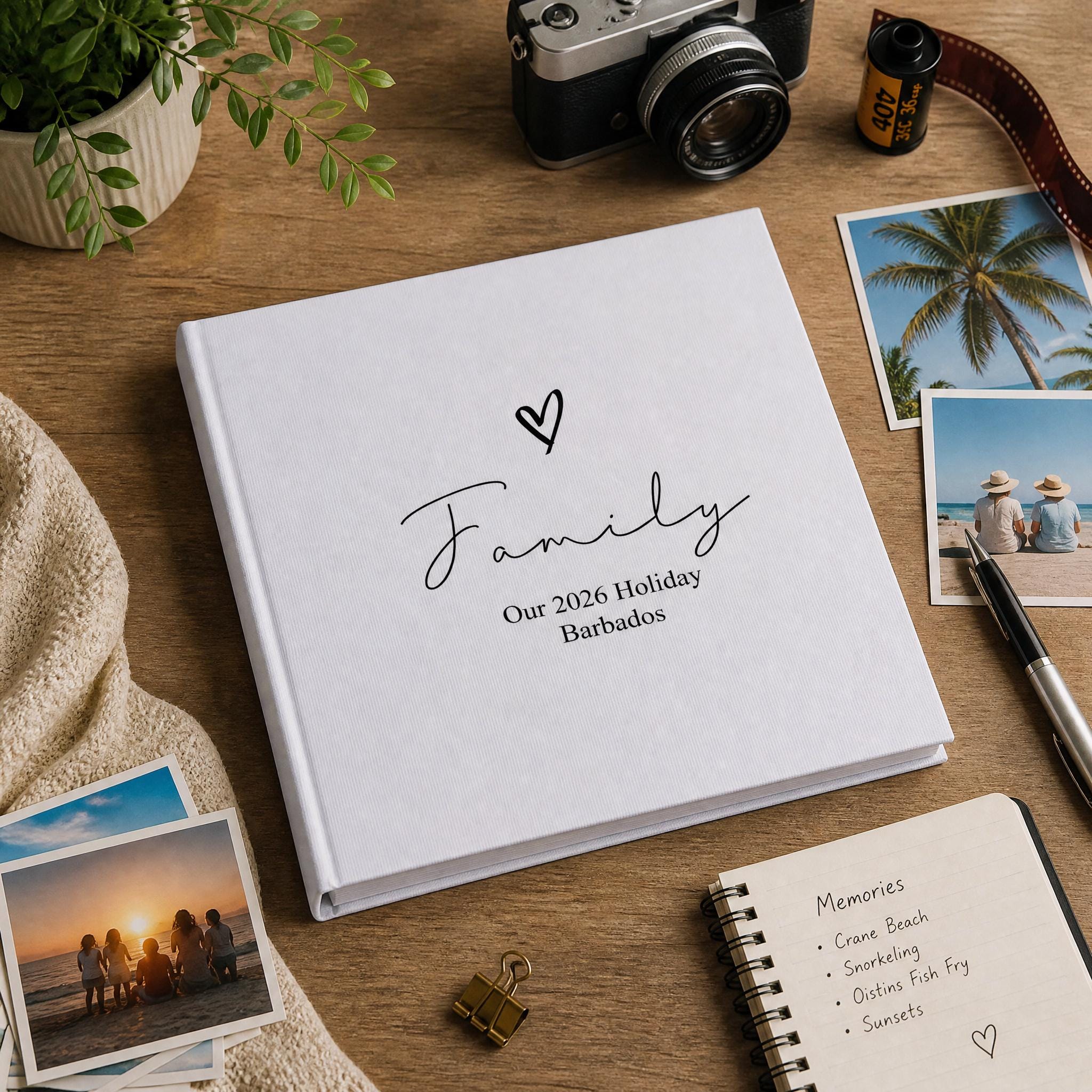 a white photo album with the title "Family" and the location "Our 2020 Holiday Barbados" on a wooden surface, surrounded by various items such as a camera, a notebook, and photographs.
