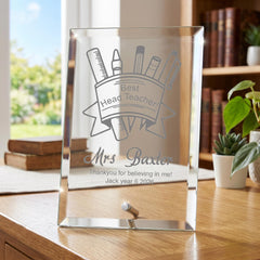 A glass picture frame on a wooden desk, displaying a personalized message for a teacher.