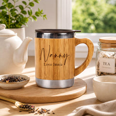 A wooden mug with the name "Nanny" and the phrase "Love Jamie" engraved on it, placed on a wooden tray next to a teapot, a jar of tea, and a small bowl of tea leaves.