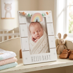 A wooden picture frame with a baby photo inside, surrounded by baby-related items such as a plush bunny, a stuffed animal, and a stack of baby blankets.