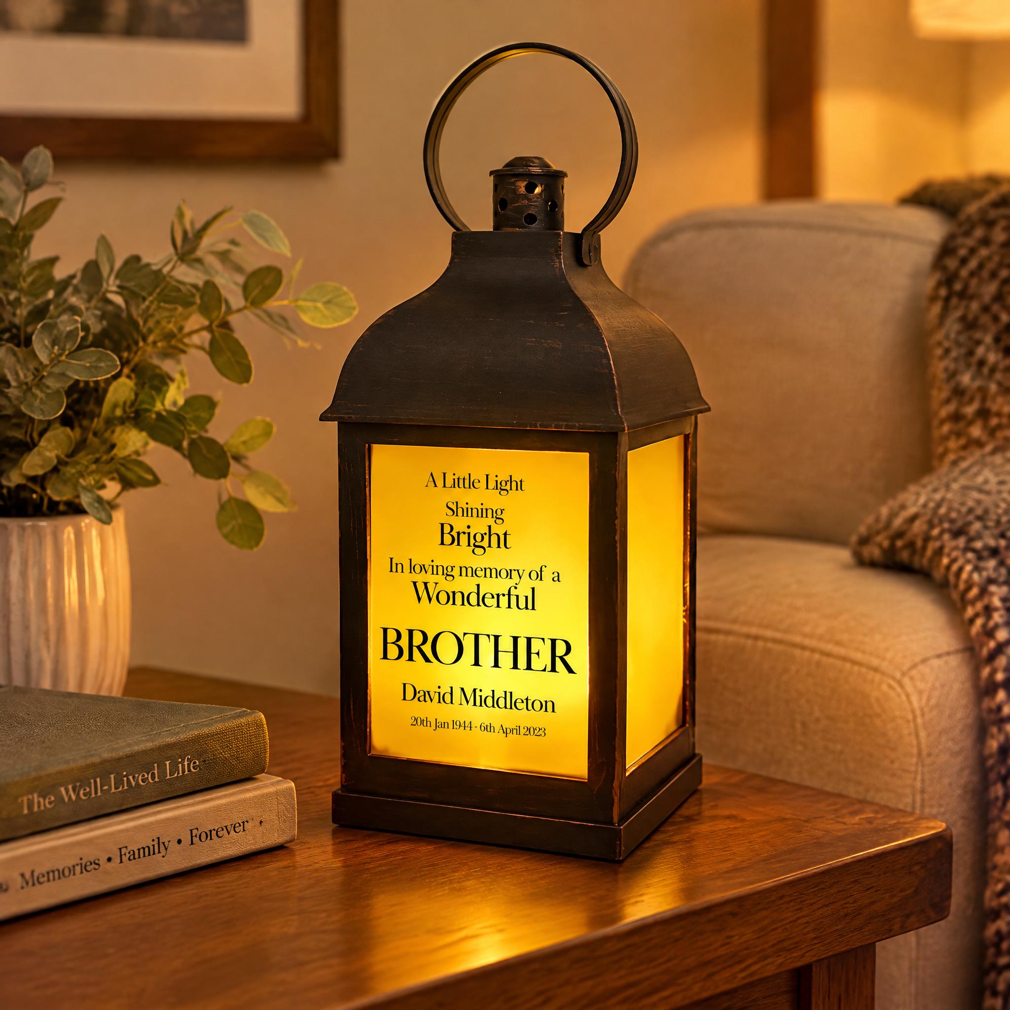 A black lantern with a yellow light on it, placed on a wooden table next to a stack of books and a potted plant.