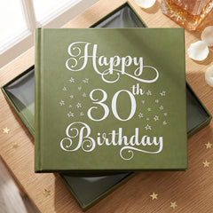 A green book titled "Happy 30th Birthday" with white stars on the cover, placed on a wooden surface with scattered gold stars around it.