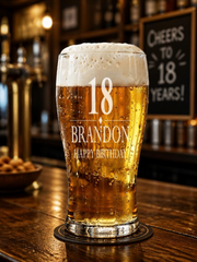A glass of beer with the number 18 and the name "Brandon" printed on it, placed on a wooden bar counter.